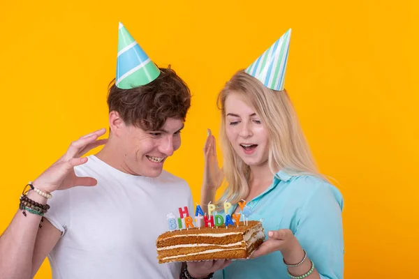 Kağıt kapaklar komik genç çift ve bir pasta ile aptal bir yüz yapmak ve sarı bir arka plan karşı dururken mutlu yıllar diliyorum. Tebrikler kavramı ve etrafında aptal. — Stok fotoğraf