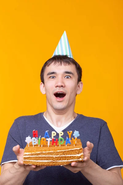 Portrait d'un drôle de type positif avec un capuchon en papier et des lunettes tenant un gâteau maison de félicitations dans ses mains sur un fond jaune. Concept et plaisir et célébration . — Photo