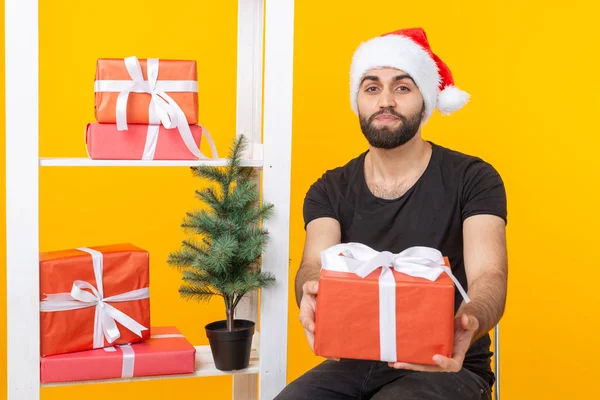 戴着圣诞老人帽子的年轻帅哥在圣诞树旁拿着祝贺礼物。圣诞节和新年假期的概念. — 图库照片
