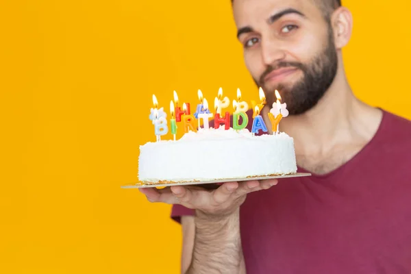 Young male hipster with a beard holding a cake with the inscription happy birthday congratulations on the anniversary and the holiday. Concept of promotions and discounts.