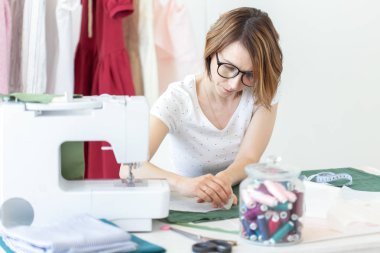 Üniversitede bir giysi tasarımcısı genç güzel kız öğrenci çalışma ve bir dikiş makinesi ile bir masada oturan ilk tezyapar. Giyim tasarım konsepti.