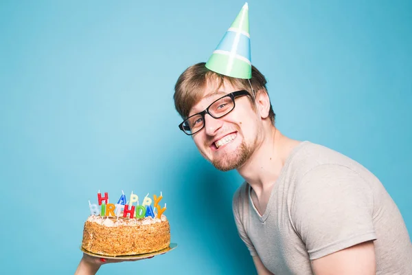 青い背景に立って幸せな誕生日ケーキとクレイジー面白い肯定的な男ヒップスター。ジョークと休日の挨拶の概念. — ストック写真