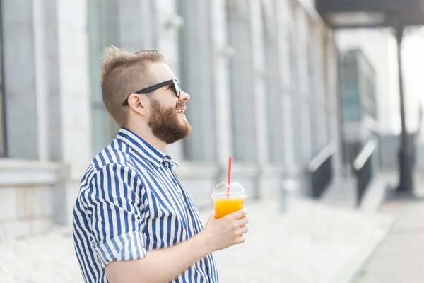 Zijaanzicht van een mooie vrolijke jonge zakenman met een stijlvolle snor en een baard met SAP in zijn handen, wandelen door de stad na een werkdag. Concept van positieve en rust. — Stockfoto