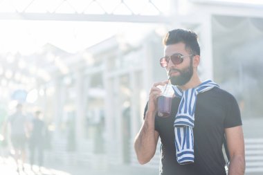 Bir bıyık ve sakal ve bir saman ile meyve suyu içme gözlük giyen sevimli şık Arap genç erkek hipster. Yaz tatili konsepti.