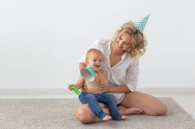 Genç gülümseyen anne ve doğum günü kapakları sevimli küçük kızı evde halı üzerinde birlikte vakit geçiriyor. Aile tatilleri ve değerleri