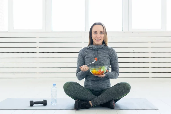 sport, healthy, people concept - Girl holding salad and dumbbell after fitness training