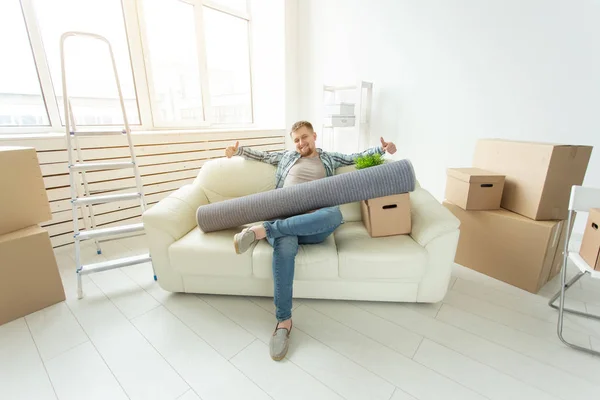 Позитивный молодой человек, сидящий на диване с вещами в новой гостиной после переезда. Концепция доступности жилья для молодежи . — стоковое фото