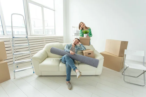 Удовлетворенные весёлая молодая пара сильный мужчина и красивая женщина держат свои вещи в руках, сидя в гостиной новой квартиры. Концепция новоселье . — стоковое фото