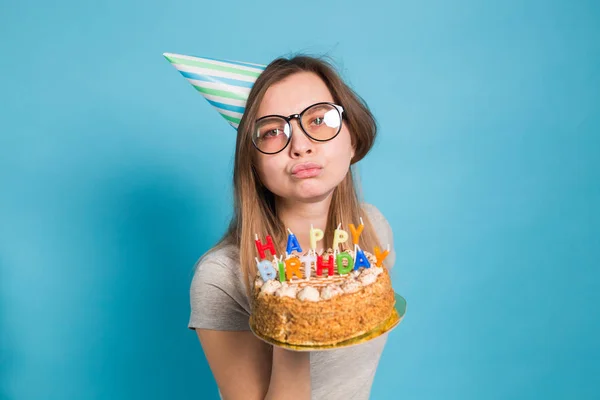 Bájos vidám őrült fiatal lány diák gratuláló papír kalap gazdaság boldog születésnapi torta a kezében állva ellen kék háttérben. Reklámfelület. — Stock Fotó