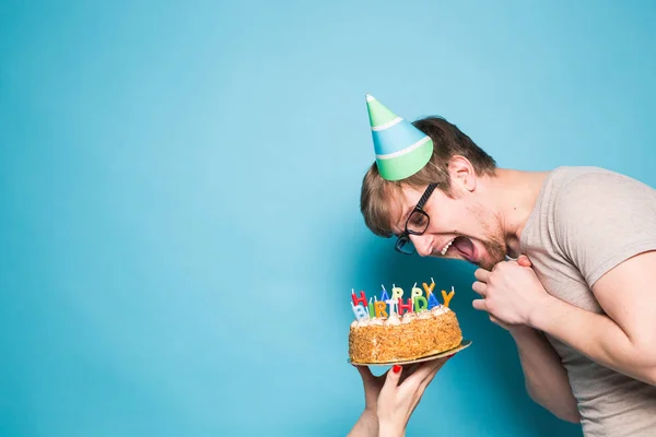 Śmieszne szalony młody człowiek w kapeluszu papier pozdrowienia chce ugryźć kawałek tort gratulacyjny. Koncepcja oszukiwanie wokół i urodzinowe pozdrowienia. Kopiuj przestrzeń — Zdjęcie stockowe
