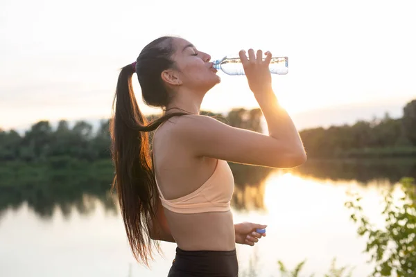 Femme athlète prend une pause, elle boit de l'eau, sur une course par une journée chaude — Photo