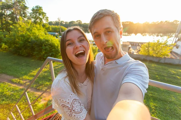 Capturar momentos brilhantes. Joyful jovem engraçado casal amoroso fazendo selfie na câmera enquanto está de pé ao ar livre — Fotografia de Stock