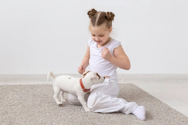 Animals, children and pets concept - little child girl sitting on the floor with cute puppy and playing