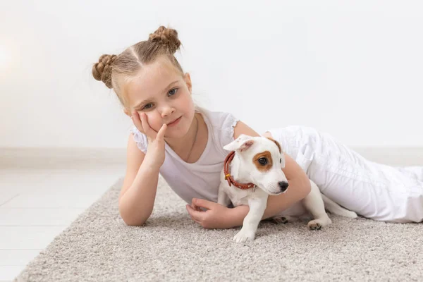 Concepto de personas, niños y mascotas - niña pequeña acostada en el suelo con un lindo cachorro Jack Russell Terrier — Foto de Stock