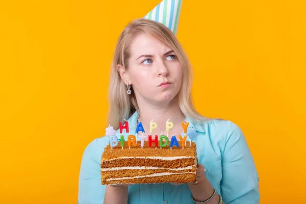 Vacances et fête accepter - Positive jeune femme tenant un gâteau d'anniversaire heureux posant sur un fond jaune . — Photo