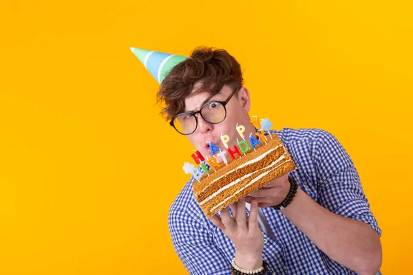 Jovem engraçado positivo com um boné e um bolo caseiro em suas mãos posando em um fundo amarelo. Aniversário e conceito de aniversário . — Fotografia de Stock