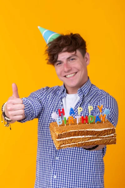 Jovem positivo segurando um bolo de aniversário feliz posando em um fundo amarelo . — Fotografia de Stock