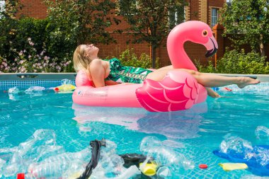 Çöp sorunu, plastik geri dönüşüm, kirlilik ve çevre kavramı - aptal kadın yüzer ve kirli bir havuzda eğlenin. Şişeler ve plastik torbalar onun yanında yüzer.