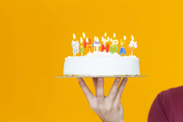 Mani che tengono una torta di compleanno con candele e il compleanno di iscrizione su uno sfondo giallo. Congratulazioni per l'anniversario e il compleanno. Copyspace . — Foto Stock