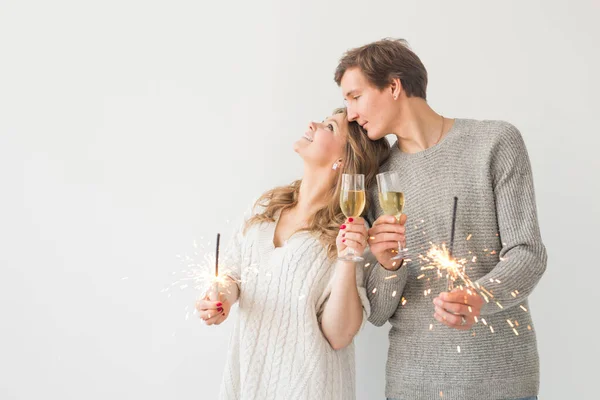 Ano Novo, feriados, data e dia dos namorados conceito - casal amoroso segurando faíscas luz e copos de champanhe sobre fundo branco com espaço de cópia — Fotografia de Stock