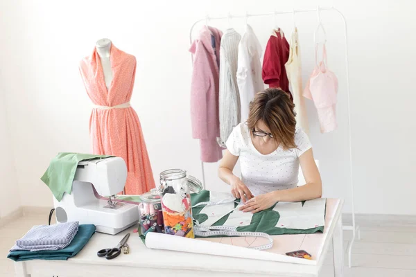 Positive junge hübsche Näherin Designerin arbeitet an einem neuen Projekt, während sie an ihrem Schreibtisch mit einer Nähmaschine in ihrer Werkstatt sitzen. Kreatives Geschäftskonzept. — Stockfoto