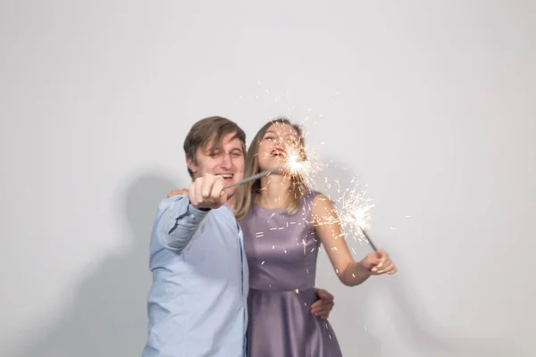 Feriados, festa e celebrações conceito - jovem casal feliz engraçado com faíscas brincando no fundo branco — Fotografia de Stock
