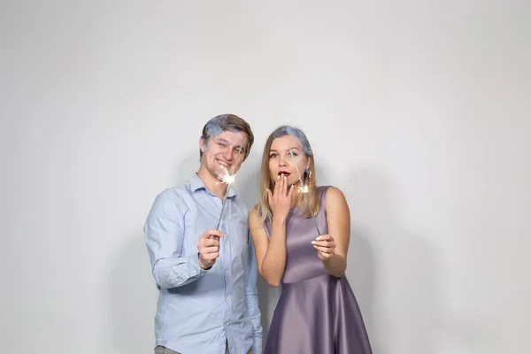 Conceito de festa, família e feriados - jovem casal olhando para faíscas no fundo branco — Fotografia de Stock