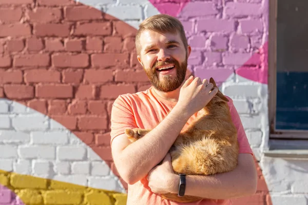 Hombre guapo está sosteniendo y abrazando lindo gato al aire libre — Foto de Stock