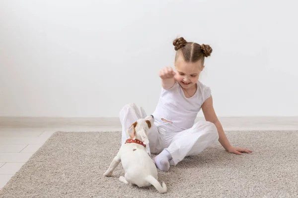 Mascotas, niños y concepto animal - Niña encantadora sentada en el suelo y alimentando al cachorro — Foto de Stock