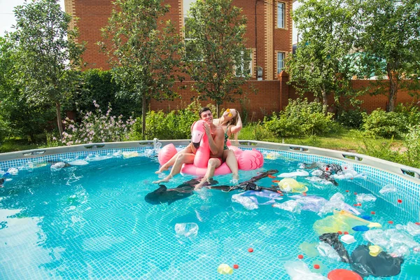 Ecology concept - Young man and woman having fun while the environment is polluted, concept of global problem with plastic rubbish floating in the water. — Stock Photo, Image