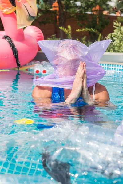 Ecology, plastic trash, environmental emergency and water pollution - desperate hoping man with a plastic bag over his head in a dirty swimming pool