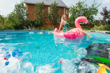 Çöp sorunu, plastik geri dönüşüm, kirlilik ve çevre kavramı - aptal kadın yüzer ve kirli bir havuzda eğlenin. Şişeler ve plastik torbalar onun yanında yüzer.