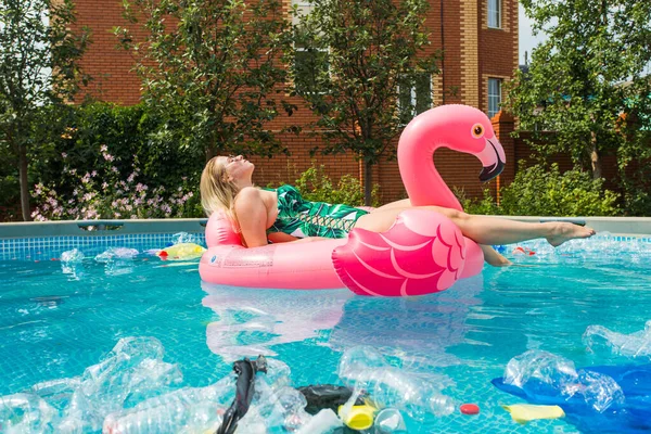 Çöp sorunu, plastik geri dönüşüm, kirlilik ve çevre kavramı - aptal kadın yüzer ve kirli bir havuzda eğlenin. Şişeler ve plastik torbalar onun yanında yüzer.