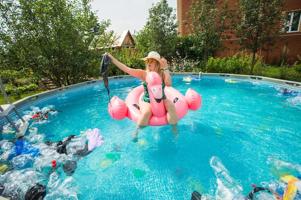 Problema de lixo, reciclagem de plástico, poluição e conceito ambiental - mulher boba nada e se divertir em uma piscina poluída. Garrafas e sacos de plástico flutuam perto dela — Fotografia de Stock