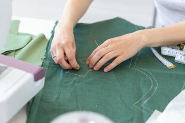 Genç bir kız tasarımcının elleri dikiş makinesi yanında masada oturan yeni bir dikiş ürünü için işaretleri yapar. Yaratıcı iş ve tasarım kavramı.