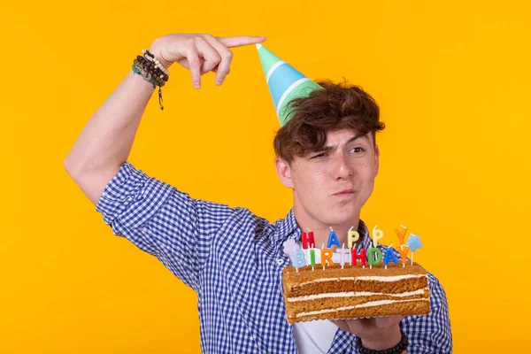 Joven divertido positivo con una gorra y un pastel casero en sus manos posando sobre un fondo amarillo. Concepto de aniversario y cumpleaños . — Foto de Stock