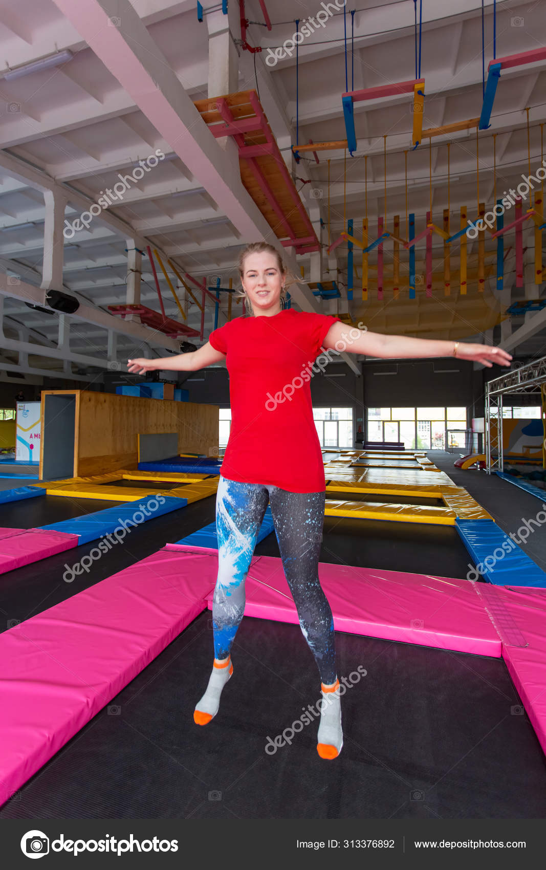 Fitness fun leisure and sport activity concept Young happy woman jumping on a trampoline indoors Stock Photo Satura 313376892