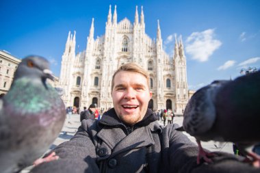 Kış seyahat, tatil ve kuşlar kavramı - yakışıklı erkek turist Milano'da ünlü Duomo Katedrali önünde selfie fotoğraf yapma komik güvercinler ile.
