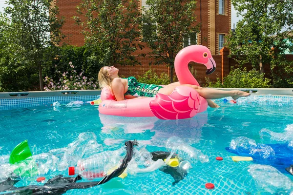 Problema de lixo, reciclagem de plástico, poluição e conceito ambiental - mulher boba nada e se divertir em uma piscina poluída. Garrafas e sacos de plástico flutuam perto dela — Fotografia de Stock