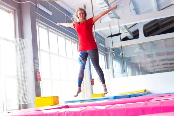 Fitness, diversión, ocio y deporte concepto de actividad - Mujer feliz joven saltando en un trampolín en el interior — Foto de Stock