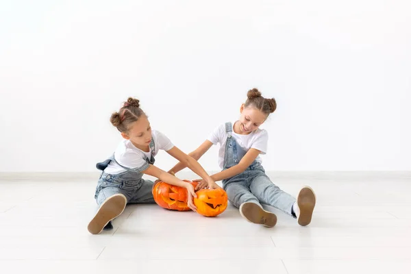 Счастливый Хэллоуин, праздники и детство - Симпатичные маленькие сестры-близнецы с маленьким Джеком-о-лансом веселятся, проводя время в помещении — стоковое фото