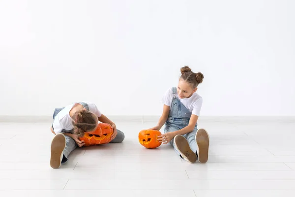 Счастливый Хэллоуин, праздники и детство - Симпатичные маленькие сестры-близнецы с маленьким Джеком-о-лансом веселятся, проводя время в помещении — стоковое фото