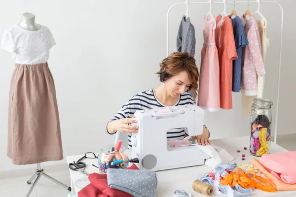 年轻的裁缝妇女缝制一个新产品在缝纫机上，坐在桌子的配件。设计师服装的概念. — 图库照片