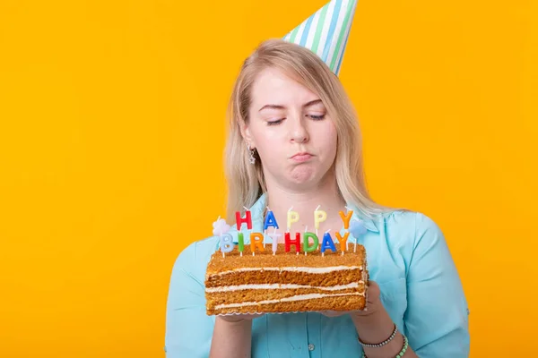 Pozytywna zabawna młoda kobieta z czapką i domowym ciastem w rękach stwarzających na żółtym tle. Koncepcja rocznicy i urodzin. — Zdjęcie stockowe
