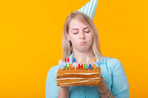 Jovem engraçada positiva com um boné e um bolo caseiro em suas mãos posando em um fundo amarelo. Aniversário e conceito de aniversário . — Fotografia de Stock