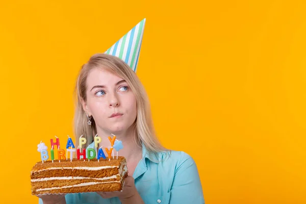 Vicces pozitív fiatal nő tartja a kezében a házi készítésű torta a felirat boldog születésnapot pózol a sárga háttérben a copyspace. Az ünnepek és évfordulók fogalma. — Stock Fotó