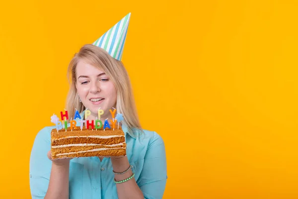 Vtipná pozitivní mladá žena drží v rukou domácí dort s nápisem Happy birthday pózování na žlutém pozadí s copyspace. Koncepce svátků a výročí. — Stock fotografie