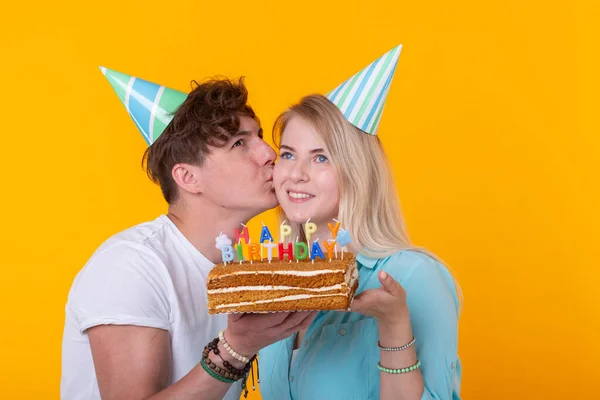 Young cheerful students charming girl and nice guy in greeting paper caps holding a cake. Concept of congratulations on the birthday and anniversary