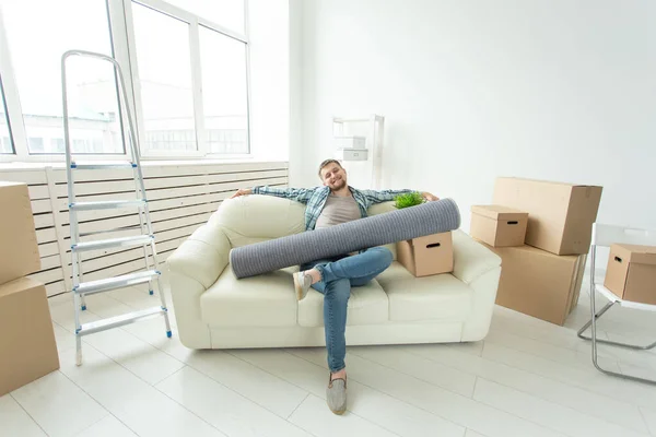 Positieve jonge man zittend op de Bank met zijn dingen in de nieuwe woonkamer na de verhuizing. Concept van de betaalbaarheid van woningen voor jongeren. — Stockfoto