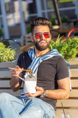 Yakışıklı genç Arap adam ahşap sopalar çin erişte tutuyor. Lezzetli Asya mutfağı konsepti.